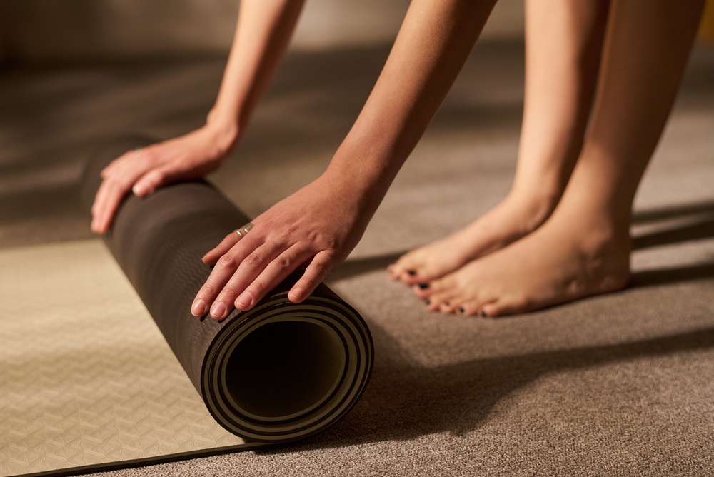 Young,Adult,Woman,Rolling,Up,Yoga,Mat,With,Both,Hands,